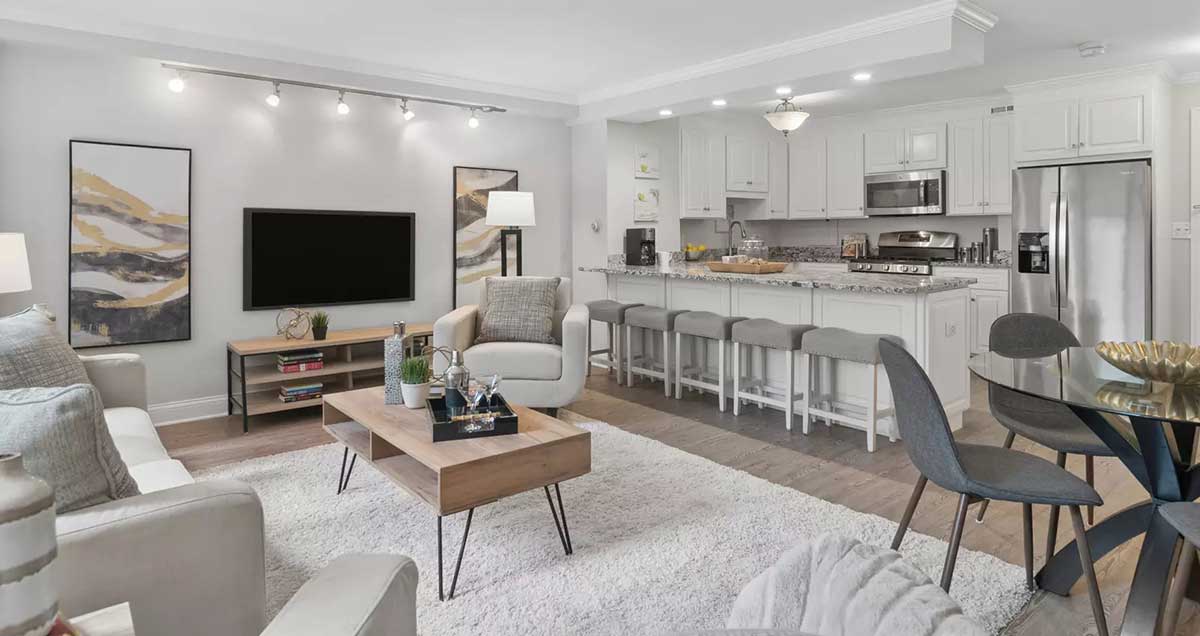 The living room, kitchen open concept at 850 North Dewitt Place Unit 4H in Chicago's Streeterville neighborhood. Listed for sale by The DelGreco Team from Coldwell Banker Realty's Lincoln Park Office. The home is all white walls and white kitchen cabinets. The living room is on the left with the open kitchen on the right.